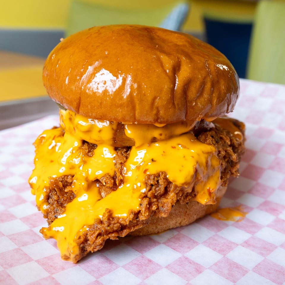 A WINGSPOT chicken sandwich with melted cheese and crispy chicken on a checkered paper.