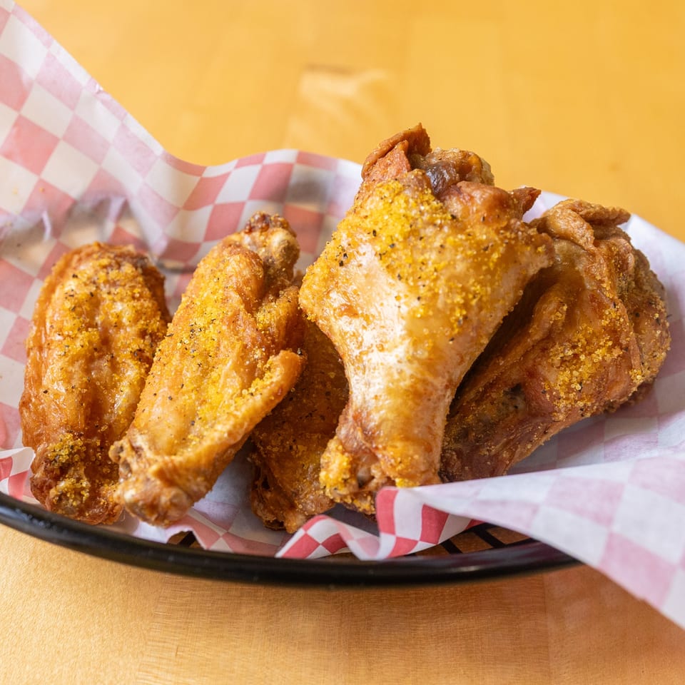 Four crispy WINGSPOT wings, seasoned with spices, served in a basket with red and white checkered paper.